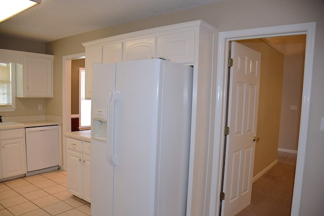 kitchen featuring light countertops, light tile patterned flooring, white cabinets, white appliances, and a sink