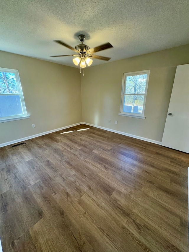 spare room with ceiling fan, dark hardwood / wood-style flooring, a textured ceiling, and a wealth of natural light