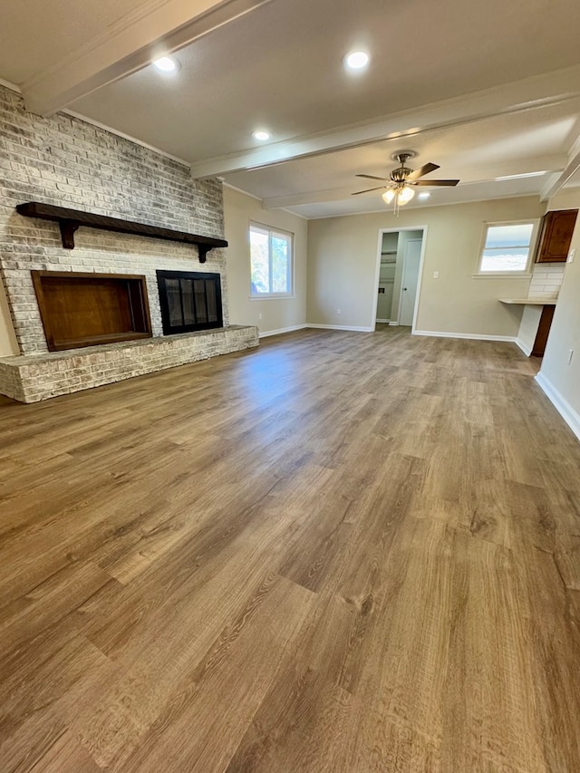 unfurnished living room featuring beam ceiling, wood-type flooring, a healthy amount of sunlight, and a fireplace