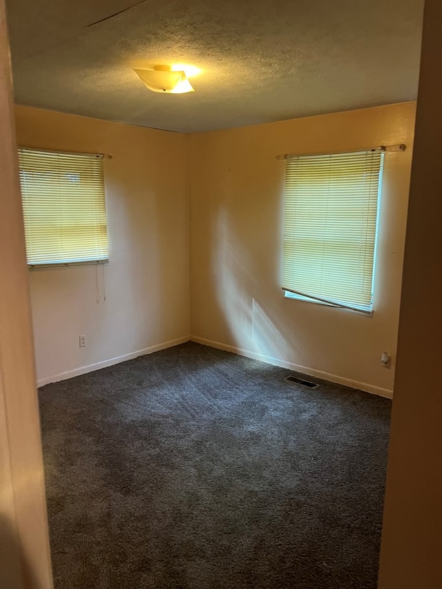 spare room featuring dark carpet and a textured ceiling