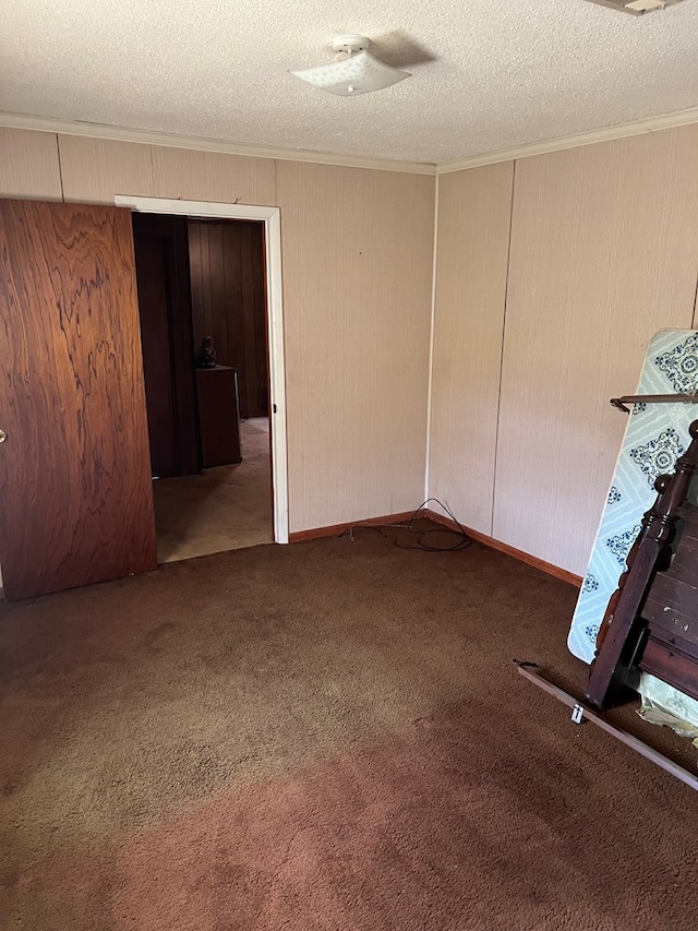 empty room featuring dark colored carpet, crown molding, and a textured ceiling