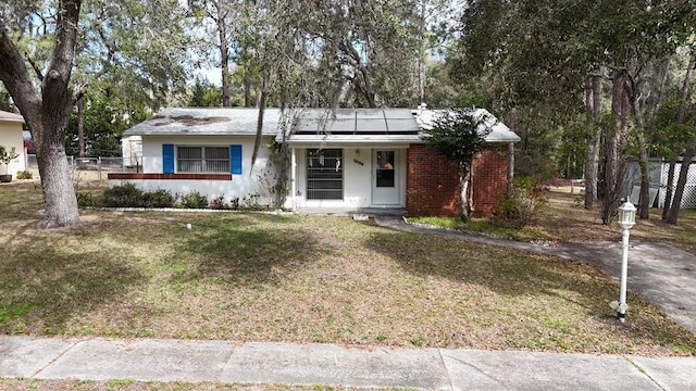 single story home with solar panels, brick siding, a front yard, and stucco siding