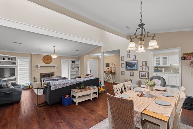 dining space featuring sink, a brick fireplace, an inviting chandelier, dark hardwood / wood-style flooring, and crown molding