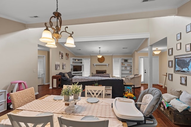 dining room with an inviting chandelier, built in features, dark hardwood / wood-style floors, crown molding, and a fireplace