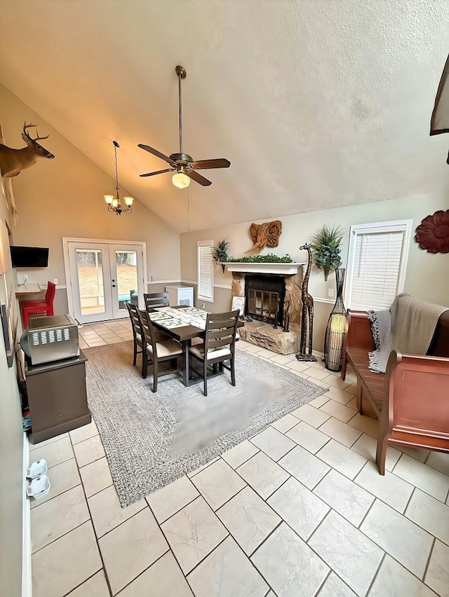 tiled dining area featuring lofted ceiling, a fireplace, french doors, a textured ceiling, and ceiling fan with notable chandelier