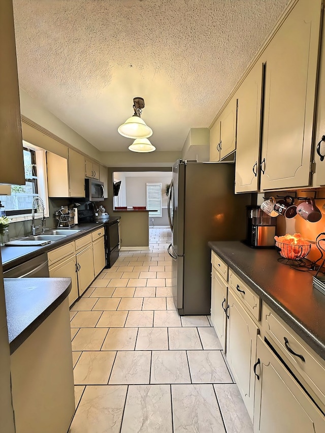 kitchen with a textured ceiling, stainless steel appliances, cream cabinetry, and sink