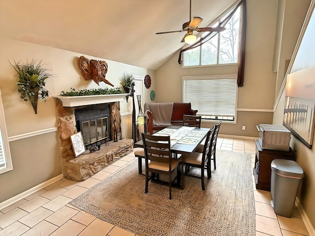 dining area featuring ceiling fan, vaulted ceiling, light tile patterned flooring, and a stone fireplace