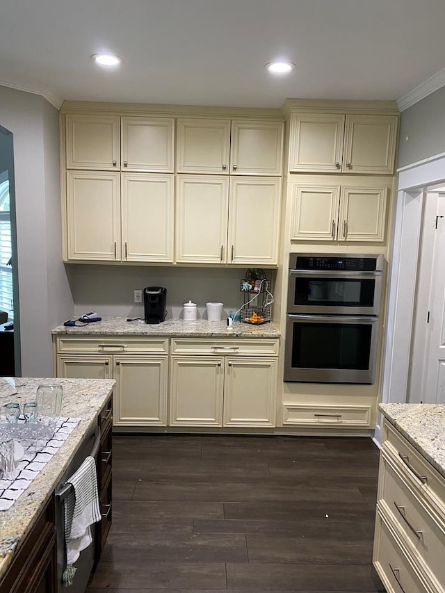 kitchen with cream cabinets, light stone counters, double oven, and ornamental molding