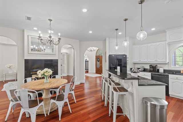 kitchen with wood-type flooring, black appliances, pendant lighting, a kitchen island, and white cabinetry