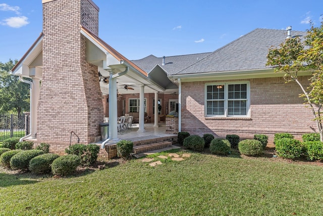 ranch-style house with a chimney, a front lawn, a patio, brick siding, and ceiling fan