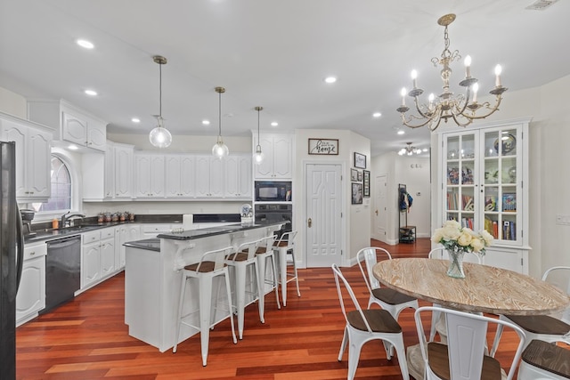 kitchen with dark countertops, a chandelier, black appliances, a kitchen island, and a breakfast bar area