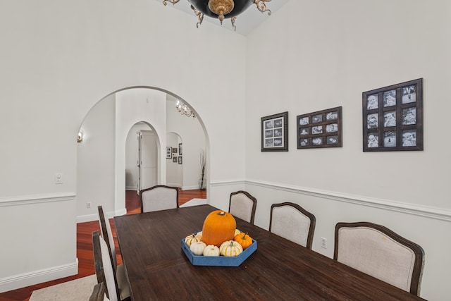 dining room featuring arched walkways, wood finished floors, a towering ceiling, and baseboards