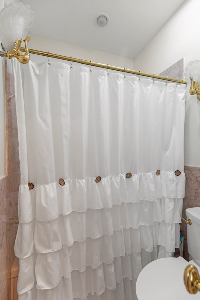 full bathroom with wainscoting, toilet, a shower with shower curtain, and tile walls