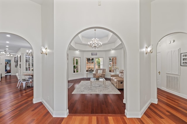 living room featuring wood-type flooring, a chandelier, a tray ceiling, and a high ceiling