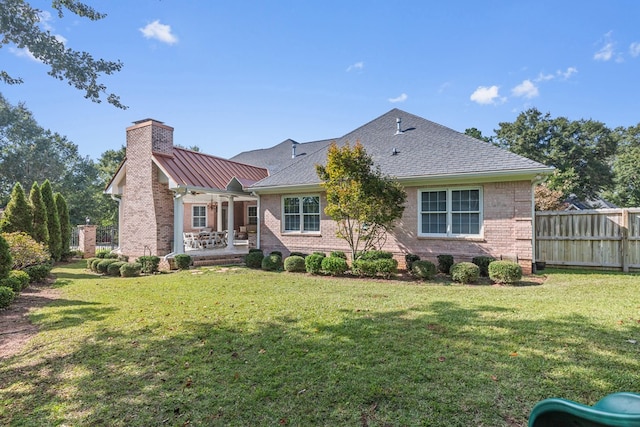 rear view of house featuring a chimney, brick siding, fence, and a lawn