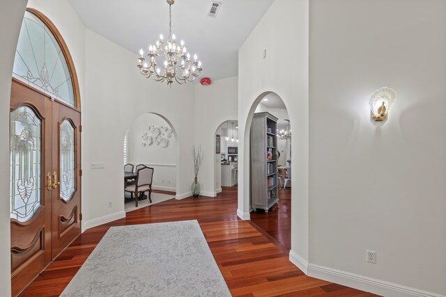 entryway featuring arched walkways, visible vents, an inviting chandelier, wood finished floors, and a high ceiling
