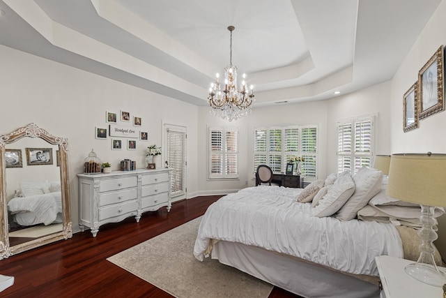 bedroom with a tray ceiling, dark wood-type flooring, and a chandelier