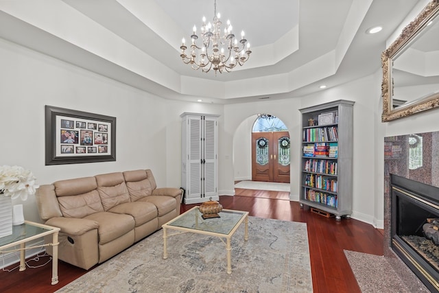 living room featuring wood finished floors, arched walkways, baseboards, a chandelier, and a tiled fireplace