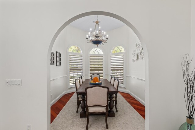 dining space with arched walkways, wood finished floors, baseboards, and an inviting chandelier