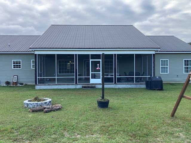 back of house featuring a lawn, a sunroom, and an outdoor fire pit