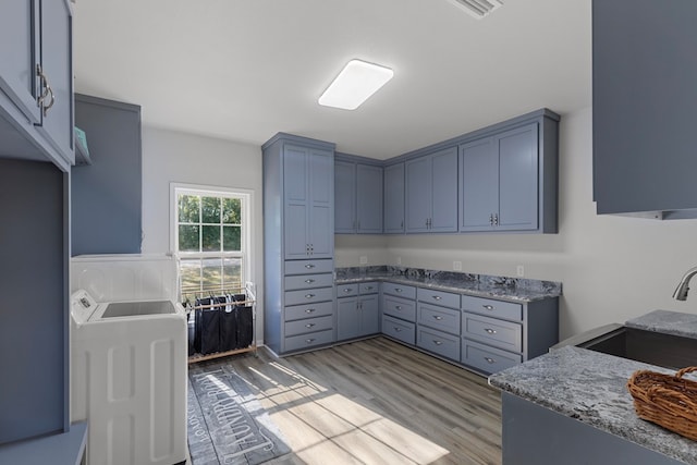 kitchen featuring light stone counters, washer / dryer, light wood-type flooring, and sink