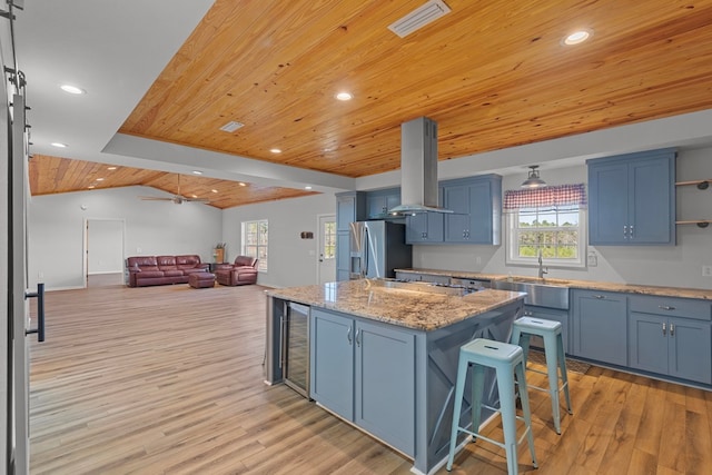 kitchen featuring stainless steel appliances, blue cabinets, a center island, vaulted ceiling with beams, and island exhaust hood