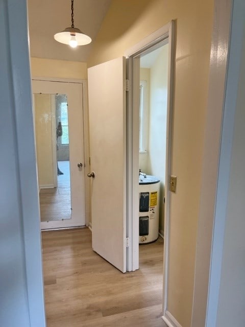 corridor featuring light wood finished floors, electric water heater, and lofted ceiling