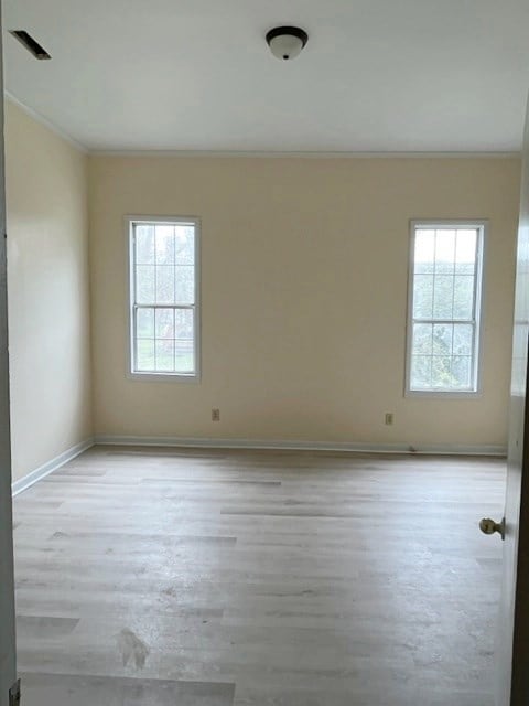 spare room with visible vents, light wood-type flooring, baseboards, and ornamental molding