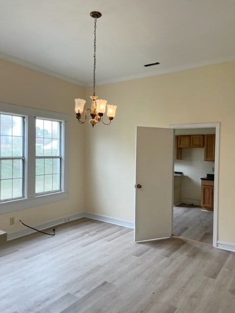 spare room featuring visible vents, baseboards, light wood-style flooring, crown molding, and a chandelier