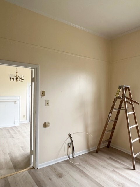 unfurnished room featuring crown molding, wood finished floors, baseboards, and a chandelier