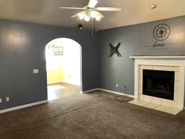 unfurnished living room featuring ceiling fan, a fireplace, arched walkways, and carpet flooring