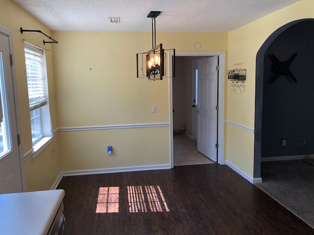 unfurnished dining area featuring arched walkways, dark wood-style flooring, visible vents, a textured ceiling, and baseboards