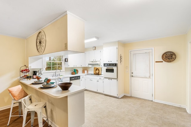 kitchen with a breakfast bar, white appliances, white cabinets, crown molding, and kitchen peninsula