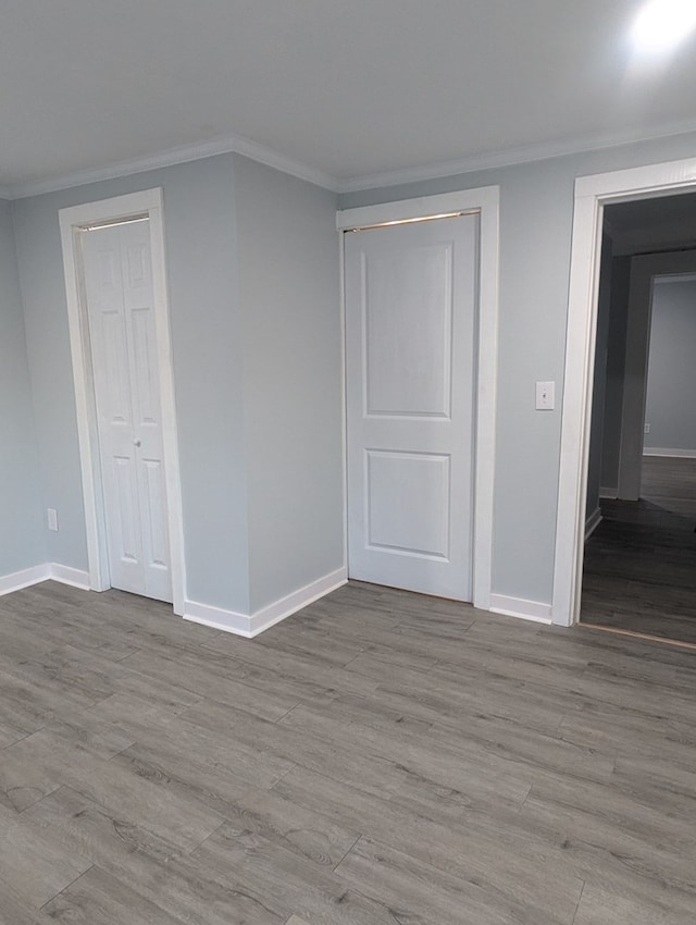 unfurnished bedroom with a closet, crown molding, baseboards, and wood finished floors