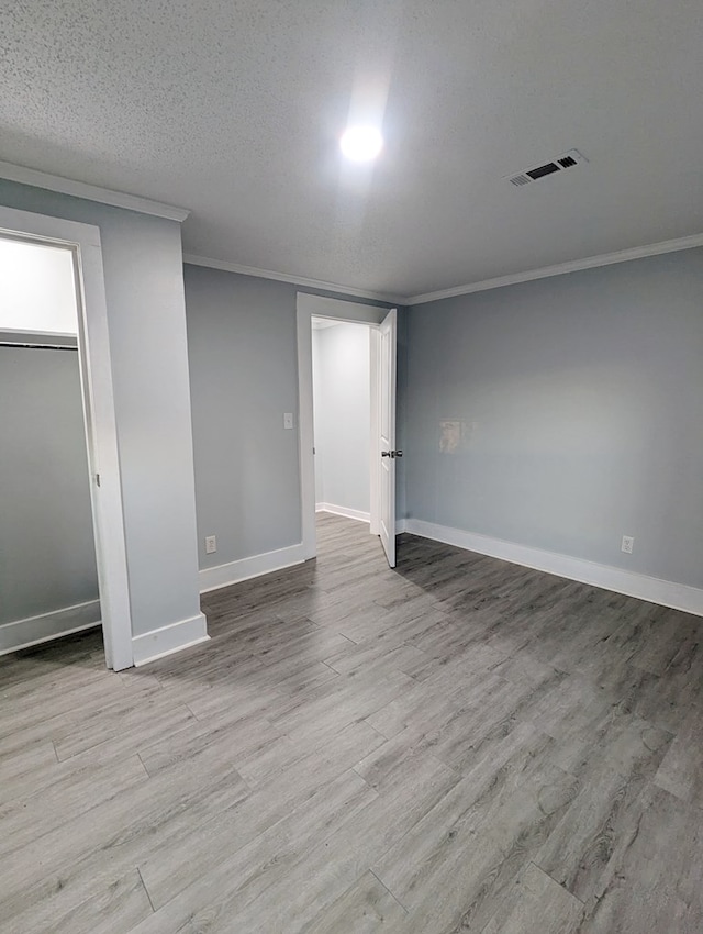 interior space featuring a textured ceiling, wood finished floors, visible vents, baseboards, and crown molding