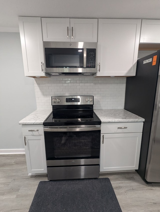 kitchen with stainless steel appliances, backsplash, light wood-style flooring, ornamental molding, and white cabinetry