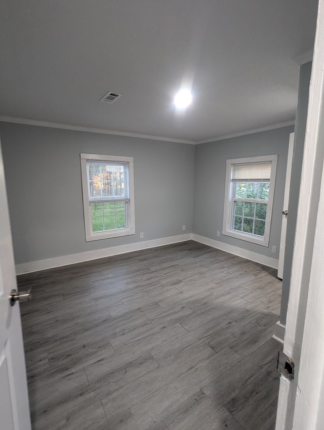 empty room with dark wood-type flooring, crown molding, and baseboards