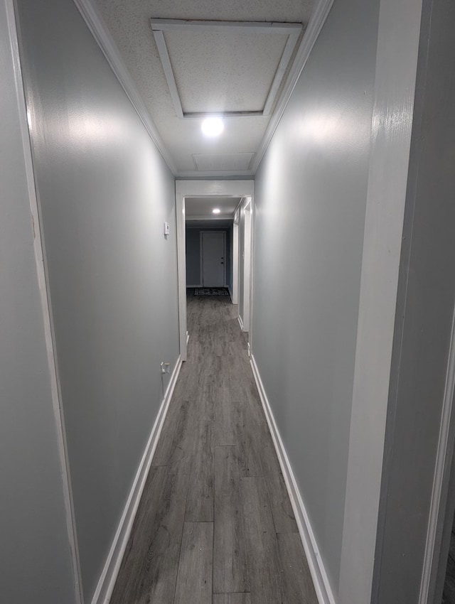 hallway with a textured ceiling, wood finished floors, baseboards, ornamental molding, and attic access