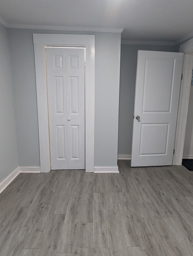 unfurnished bedroom featuring baseboards, a closet, wood finished floors, and crown molding