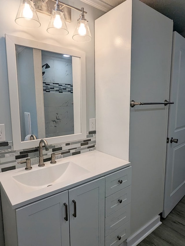 full bath featuring wood finished floors, vanity, baseboards, a tile shower, and backsplash