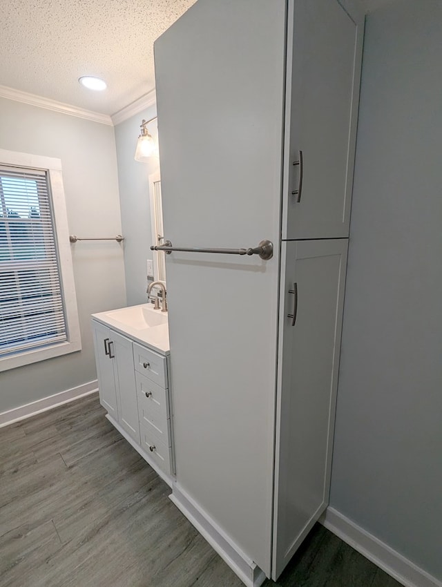 bathroom with ornamental molding, a textured ceiling, vanity, wood finished floors, and baseboards