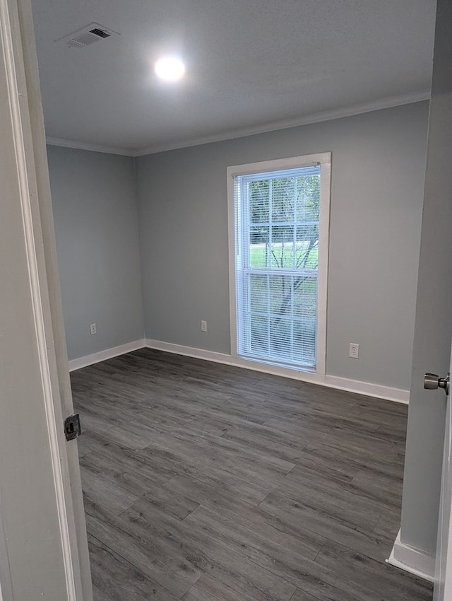 spare room featuring baseboards, visible vents, dark wood-style flooring, and crown molding