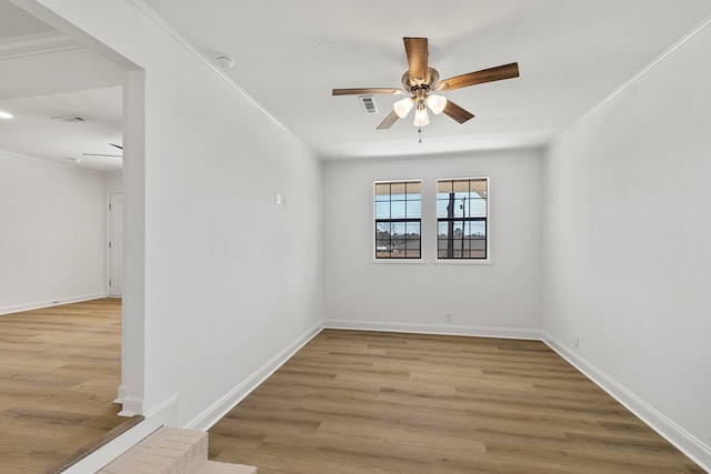 empty room featuring visible vents, crown molding, baseboards, and wood finished floors