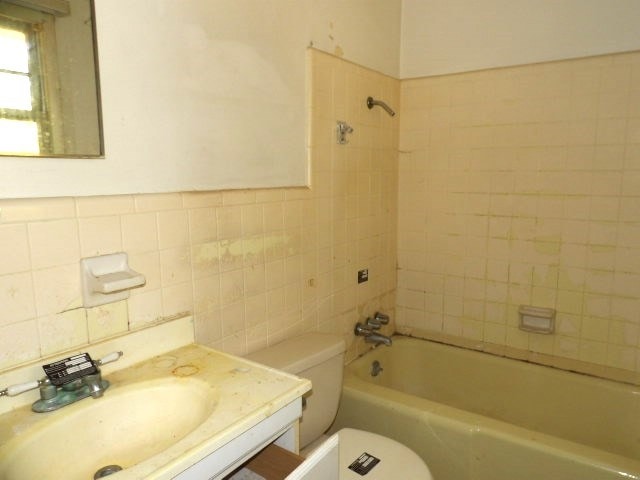 bathroom featuring shower / bathing tub combination, a sink, toilet, and tile walls