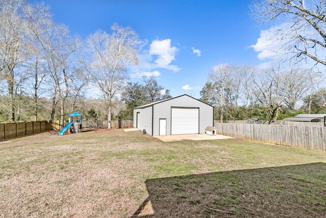 view of yard with a fenced backyard, a detached garage, a playground, and an outbuilding