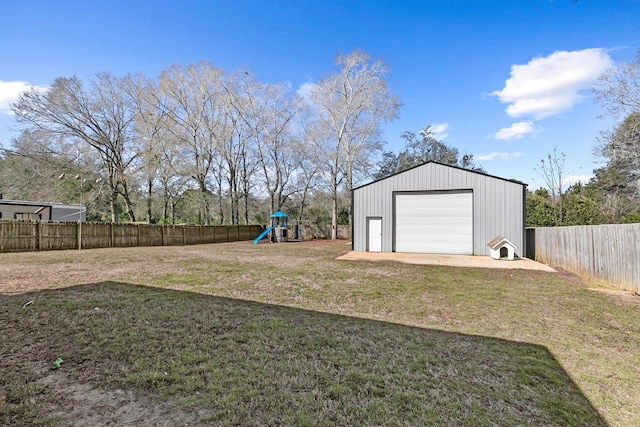 view of yard with driveway, a playground, a fenced backyard, and a detached garage