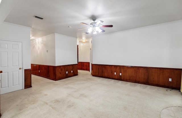 carpeted empty room with ceiling fan, crown molding, and wood walls