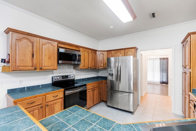 kitchen featuring tile counters, backsplash, crown molding, light tile patterned floors, and appliances with stainless steel finishes