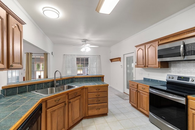 kitchen with appliances with stainless steel finishes, ceiling fan, crown molding, sink, and tile counters