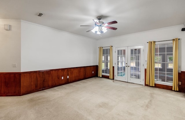 empty room featuring wood walls, french doors, ceiling fan, ornamental molding, and light colored carpet